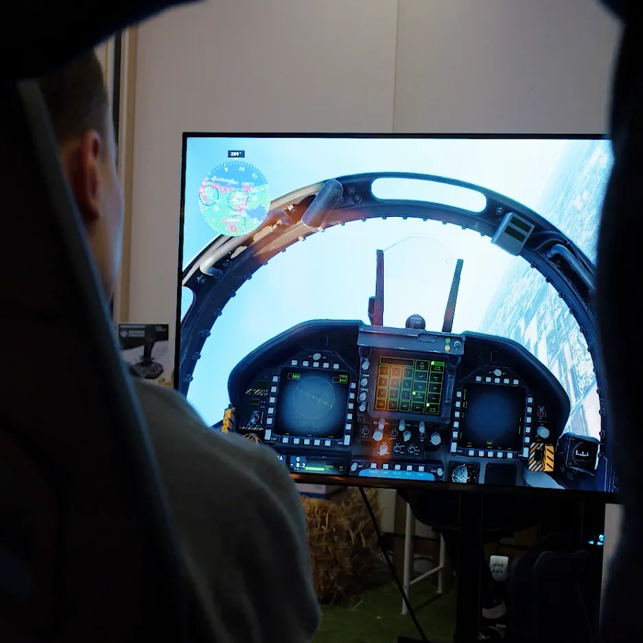 A visitor at the controls of a flight simulator, a jet cockpit on the screen in front of them